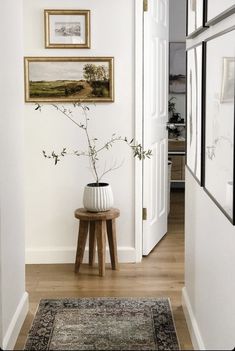 a white vase sitting on top of a wooden table next to a doorway with pictures above it