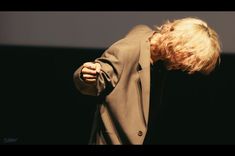 a man with blonde hair wearing a suit and holding his hands to his face while standing in front of a screen