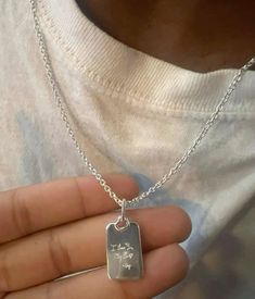 a person holding a silver dog tag on a chain