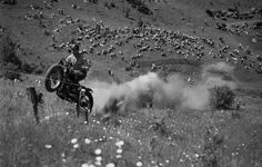 a man riding on the back of a dirt bike over a grass covered hill next to a crowd of people