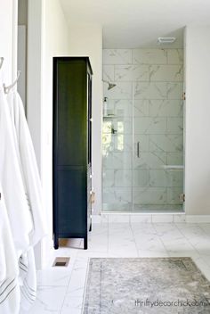 a white bathroom with marble flooring and black cabinetry, along with a walk - in shower