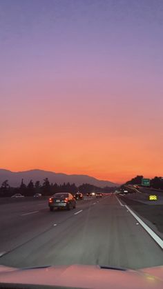 cars driving down the highway at sunset with mountains in the background