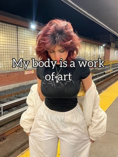 a woman with red hair is standing in front of a train platform and has her back to the camera