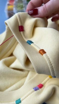 someone is stitching something on top of a shirt with colorful threads and needles