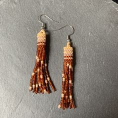 the beaded tassel earrings are hanging from hooks on a stone slab with a black background