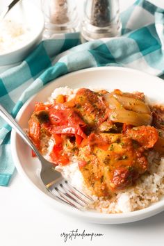 a white plate topped with rice and meat covered in sauce on top of a blue checkered table cloth