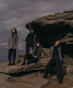 four people are sitting on rocks in front of the ocean and one is wearing a gray coat