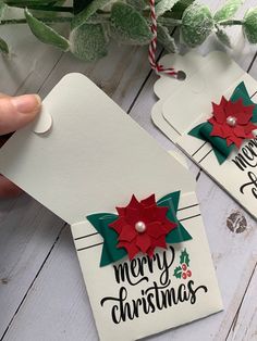 two christmas gift tags with poinsettis and holly on them are being held by someone's hand