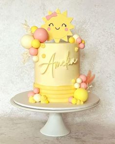 a yellow and pink birthday cake on a white pedestal with an embellished name