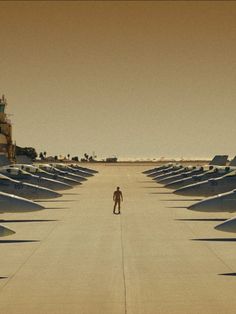 a man standing in the middle of an empty parking lot surrounded by rows of planes