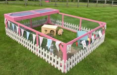 a pink and white fenced in area with a small dog house on the grass