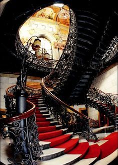 an ornate staircase with red carpet and wrought iron handrails, leading up to the second floor