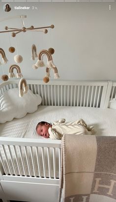 a baby laying in a white crib next to a blanket and some toys hanging from the ceiling