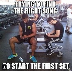 two men sitting on benches in a gym using their cell phones and texting, trying to find the right song so start the first set