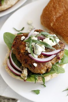 a burger with onions, lettuce and feta cheese is on a white plate