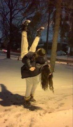 two people standing in the snow with their arms around each other and one person holding onto a tree