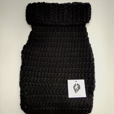 a black crocheted dog coat with a white tag on it