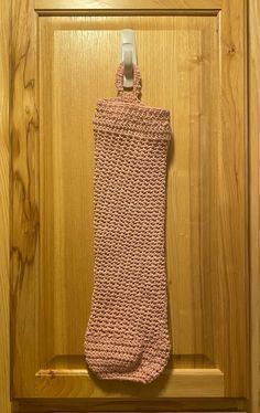 a pink crocheted sock hanging from a hook on a wooden door frame with wood paneling