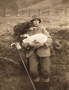 an old black and white photo of a boy holding a dog in his arms while standing on the side of a hill