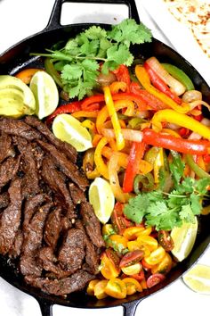 a skillet filled with steak, peppers and cilantros on top of a table