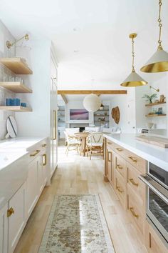 a kitchen with wooden floors and white walls, gold accents on the cabinets and brass pendant lights