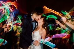 a bride and groom kissing in front of colorful lights