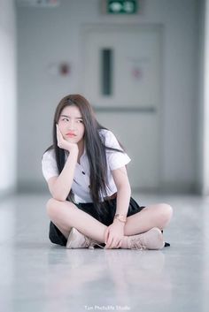 a young woman sitting on the floor with her hand under her chin and looking at the camera