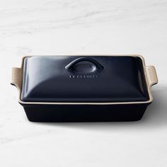 a black rectangular casserole dish on a white marble countertop with the word lactchett written in gold