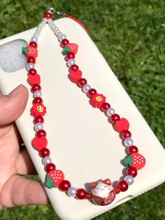 a hand holding a cell phone with a red and white beaded necklace on it