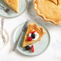 two slices of pie on plates next to whipped cream and berries with forks in the foreground