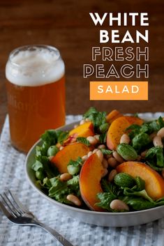 a salad with peaches and spinach in a bowl next to a glass of beer