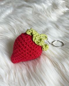 a crocheted strawberry keychain is laying on white fur