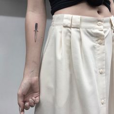 a woman with a knife tattoo on her left arm and the other hand behind her back