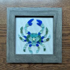 a crab made out of sea glass sitting in a frame on a wooden table next to a wall