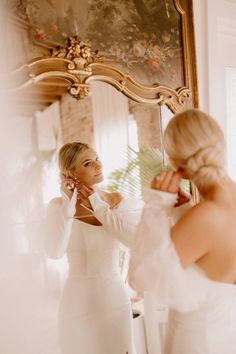 a woman in a white dress looking at herself in the mirror