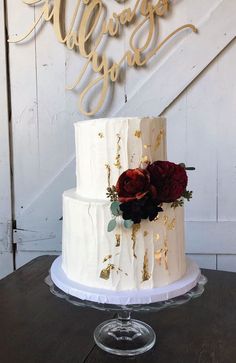 a white wedding cake with red flowers on top and the words always you are spelled in gold lettering