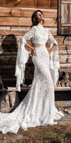 a woman standing in front of a wooden building wearing a white wedding dress with long sleeves