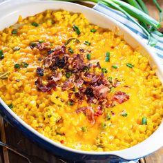 a casserole dish with corn and bacon in it on a wooden table next to green onions