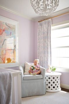 a baby sitting in a chair with a book on it's lap next to a window