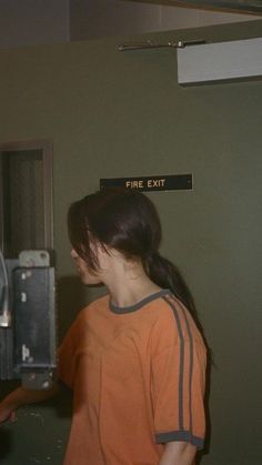 a woman standing in front of a fire exit sign with her hand on the door