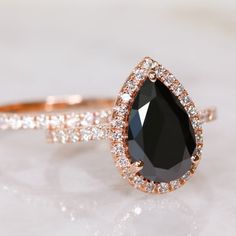 an engagement ring with a pear shaped black diamond surrounded by white and rose gold diamonds