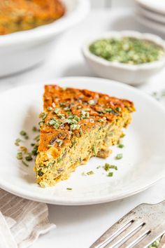 a slice of quiche on a white plate next to silverware and napkins