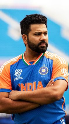 a man with his arms crossed standing in front of a blue and orange stadium background