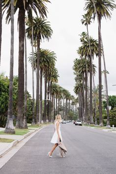 a woman crossing the street in front of palm trees