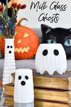 two white ghost vases sitting next to each other on top of a book with pumpkins in the background