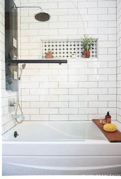 a bathtub with a wooden tray and soap on the side next to it is decorated with black and white tiles