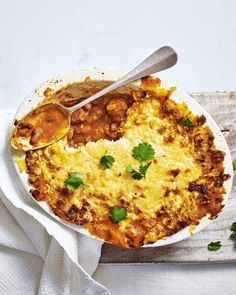 a white plate topped with an omelet covered in cheese and sauce next to a spoon