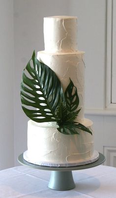 a three tiered white cake with green leaves on top