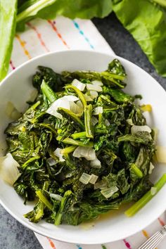 a white bowl filled with greens and onions on top of a striped cloth next to a fork