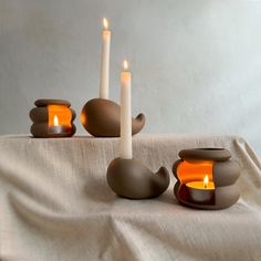 three candles sitting on top of a table next to two tea light holders and one candle holder